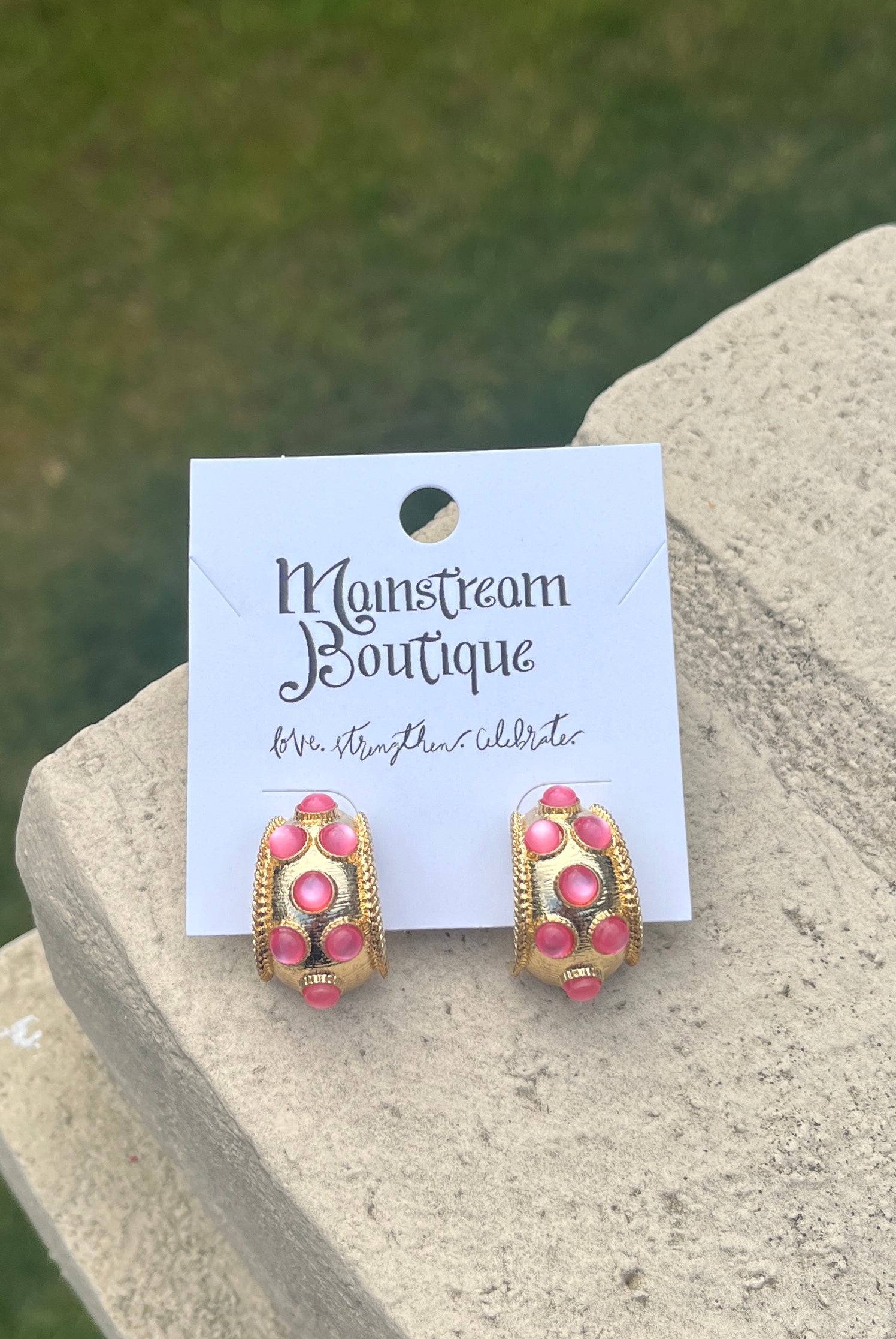 Pair of pink and gold earrings against a natural background.