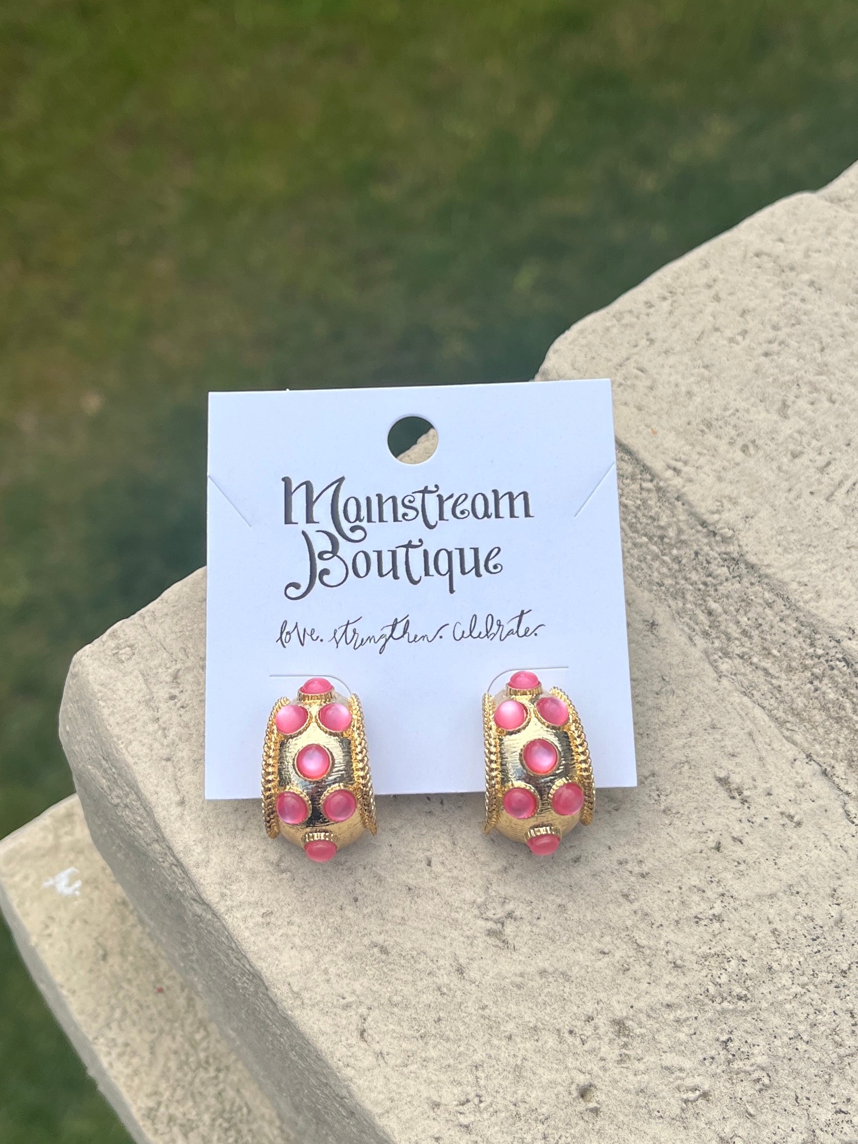 Pair of pink and gold earrings against a natural background.