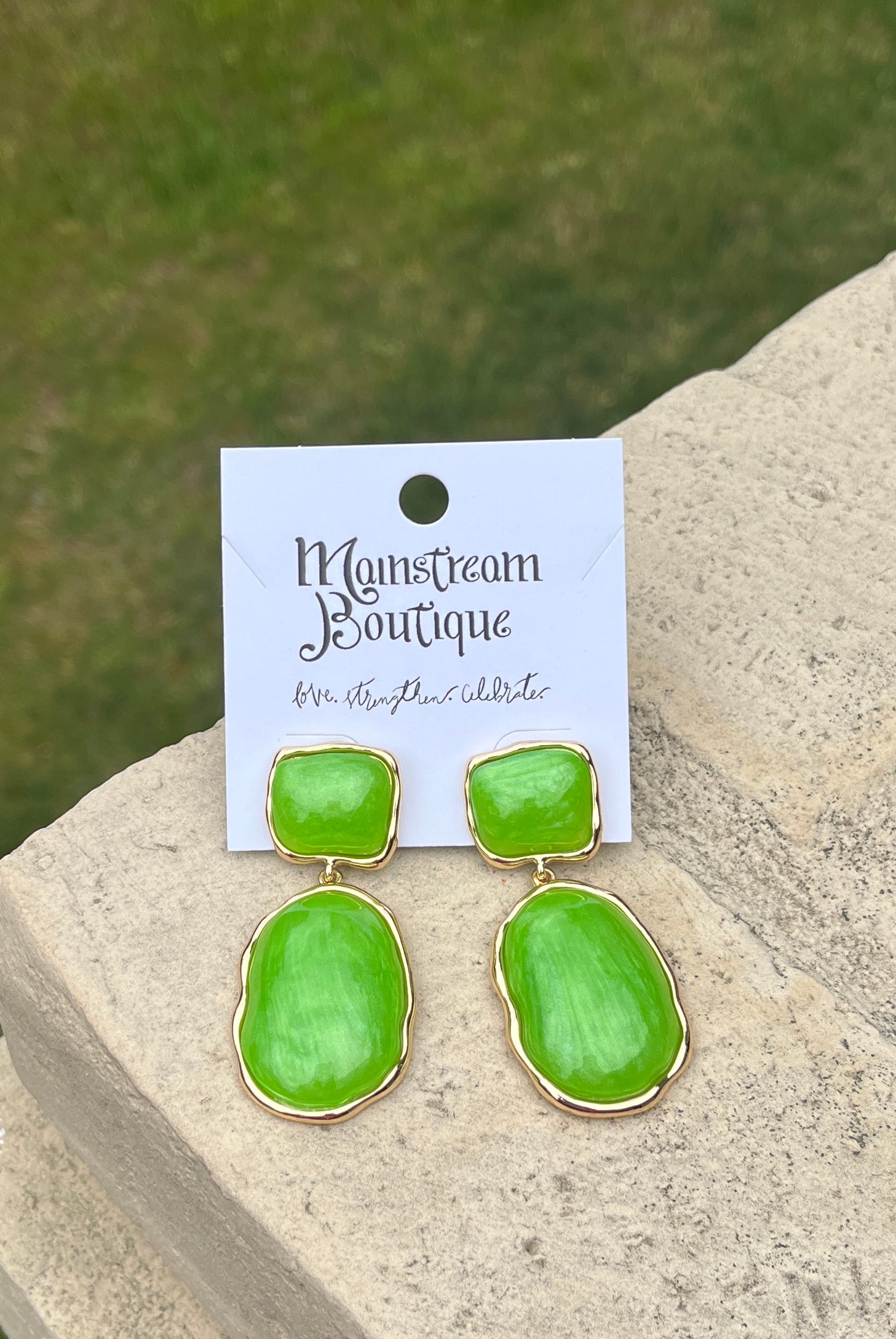 Green earrings placed on a stone surface.