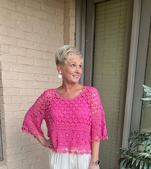 Woman wearing a pink crochet top standing outside a building.