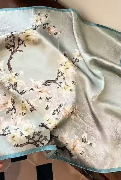 Silk scarf with floral design held by a hand on a wooden surface
