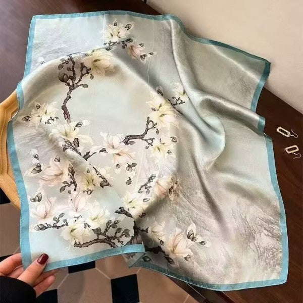 Silk scarf with floral design held by a hand on a wooden surface