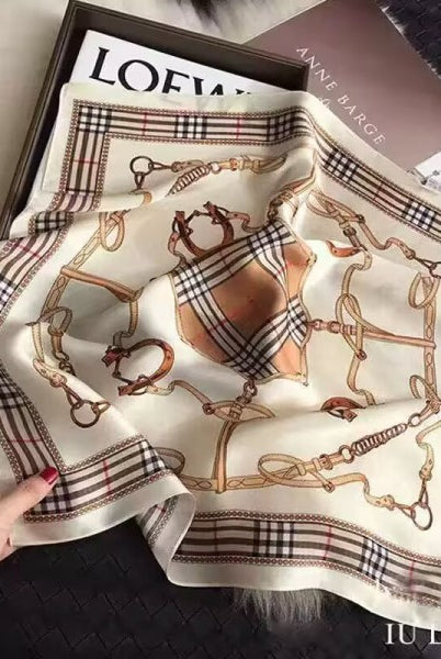 Burberry scarf with horse and harnais pattern held by a hand on a textured surface.