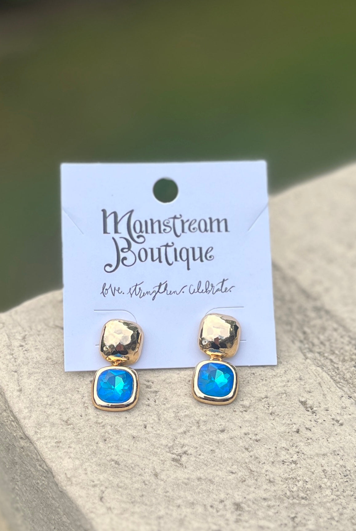 Gold and piercing blue earrings placed on a stone surface.