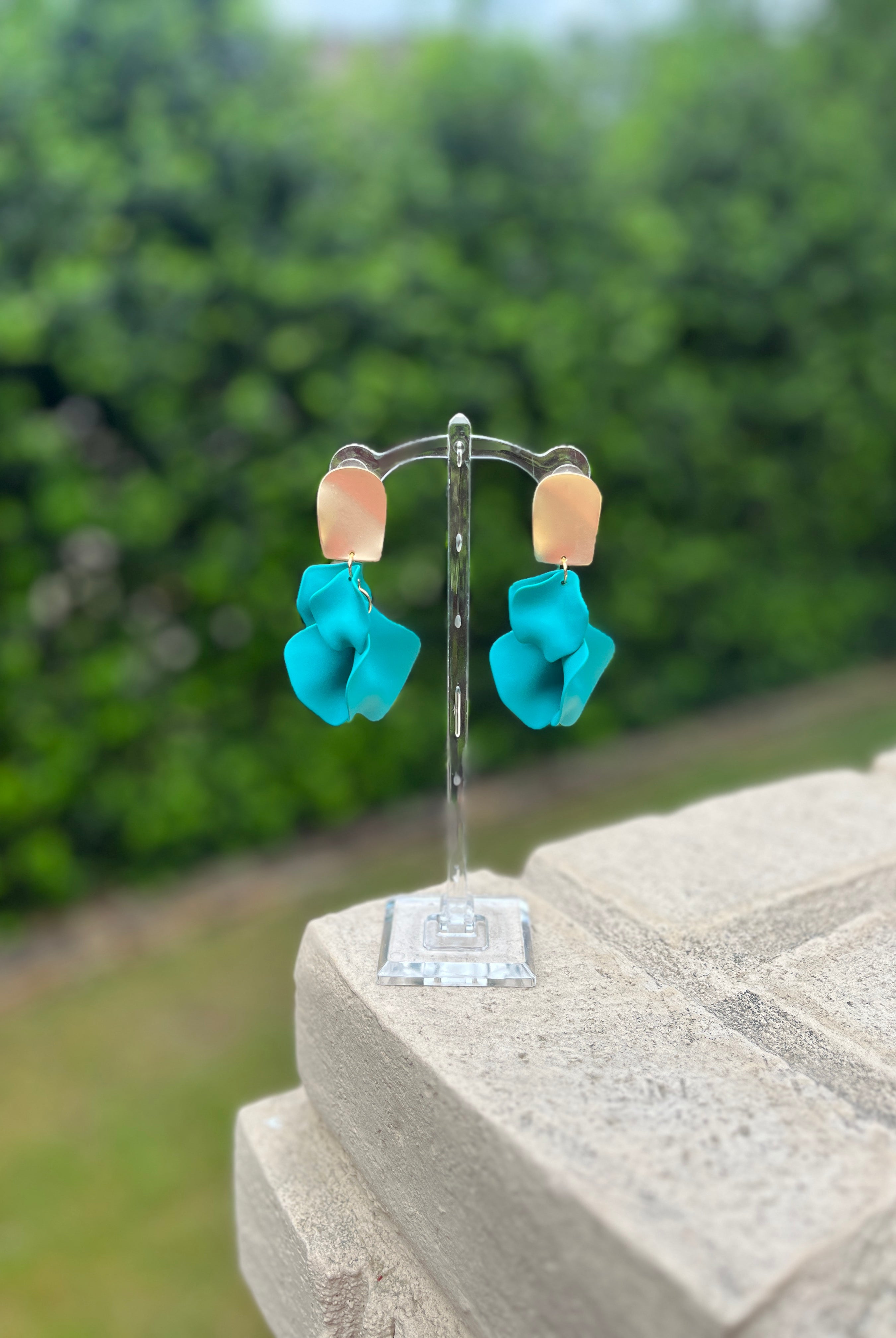 Turquoise flower-shaped earrings on a stand with a blurred green background