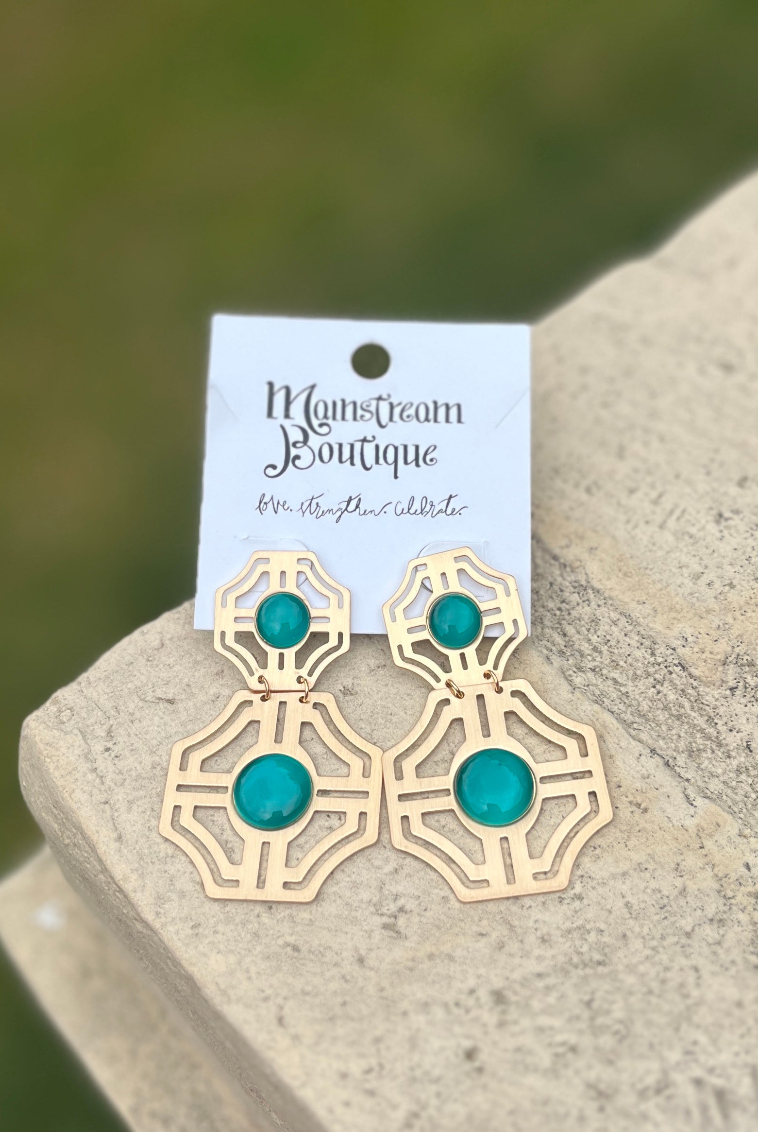 Gold earrings with turquoise stones placed on a stone surface.