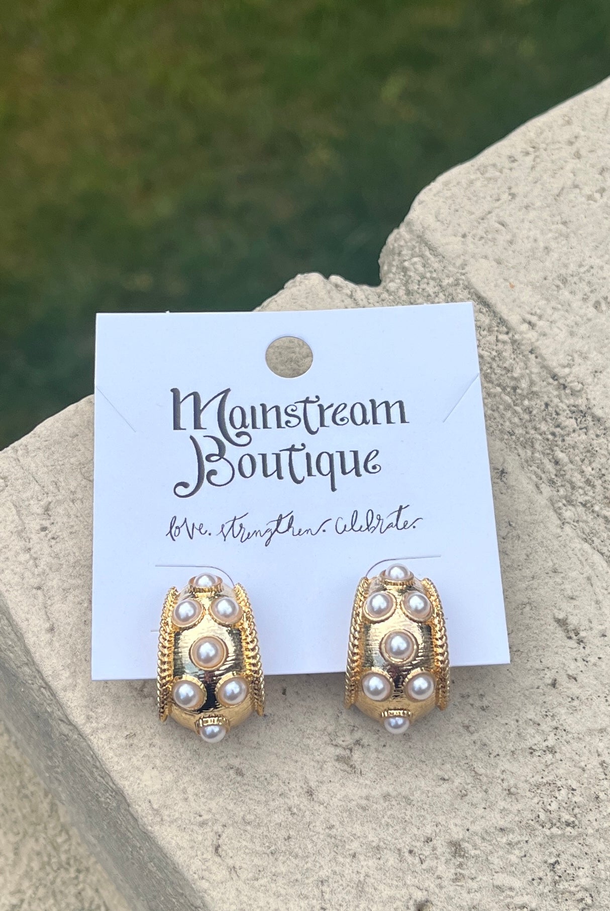 Gold and pearl earrings placed on a stone surface.