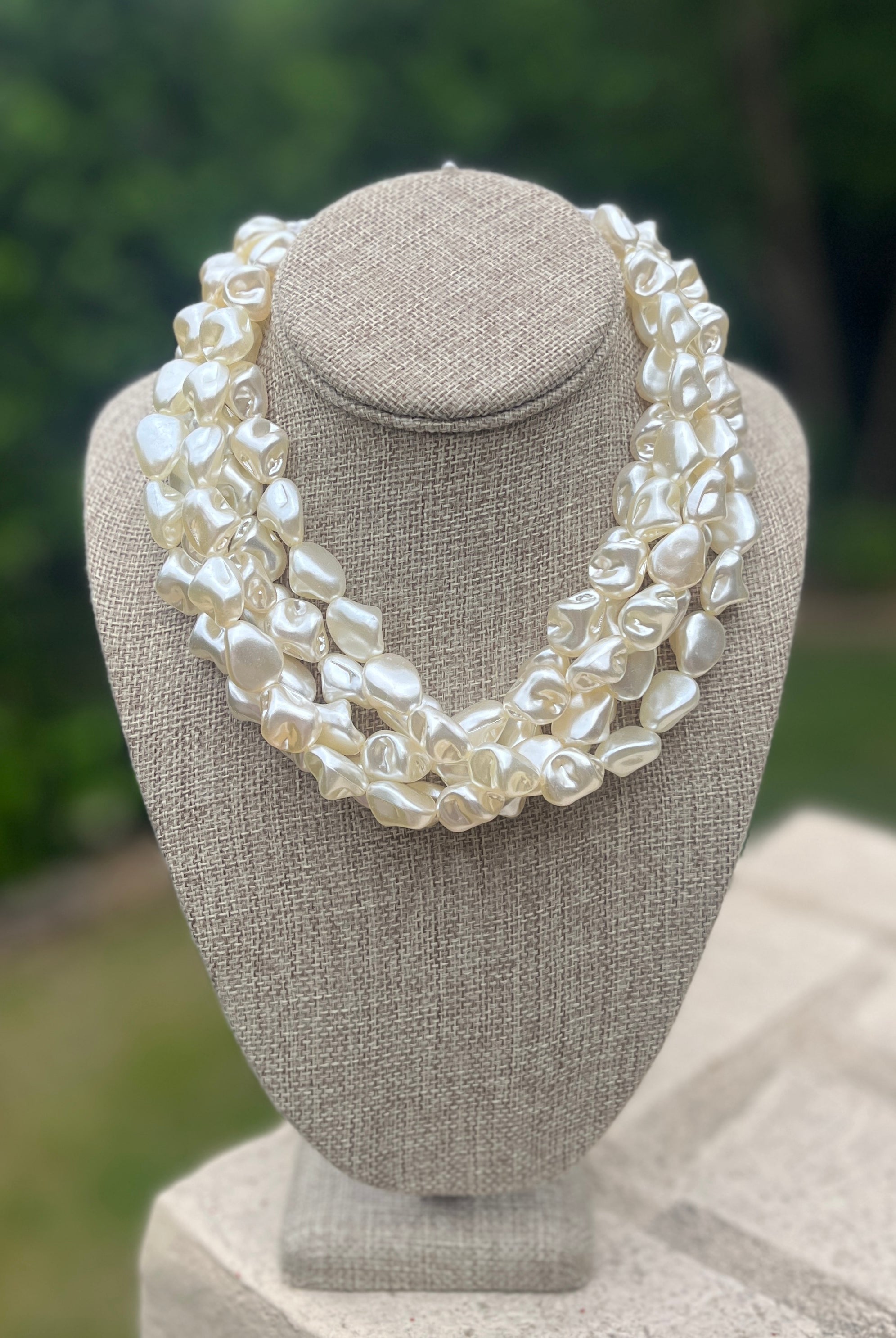 White pearl necklace on a gray bust with a blurred green background