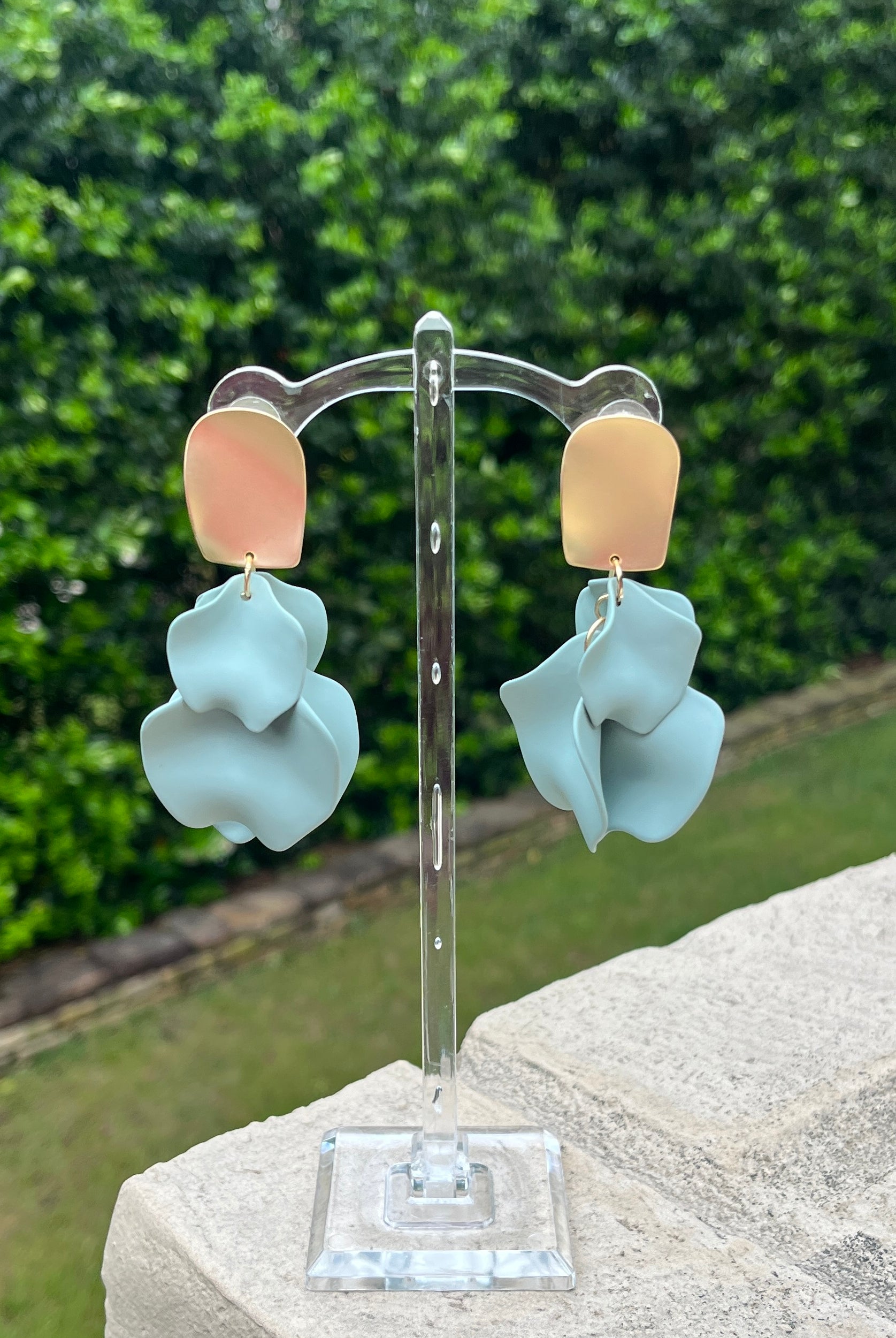 Pair of earrings on a stand with a green outdoor background