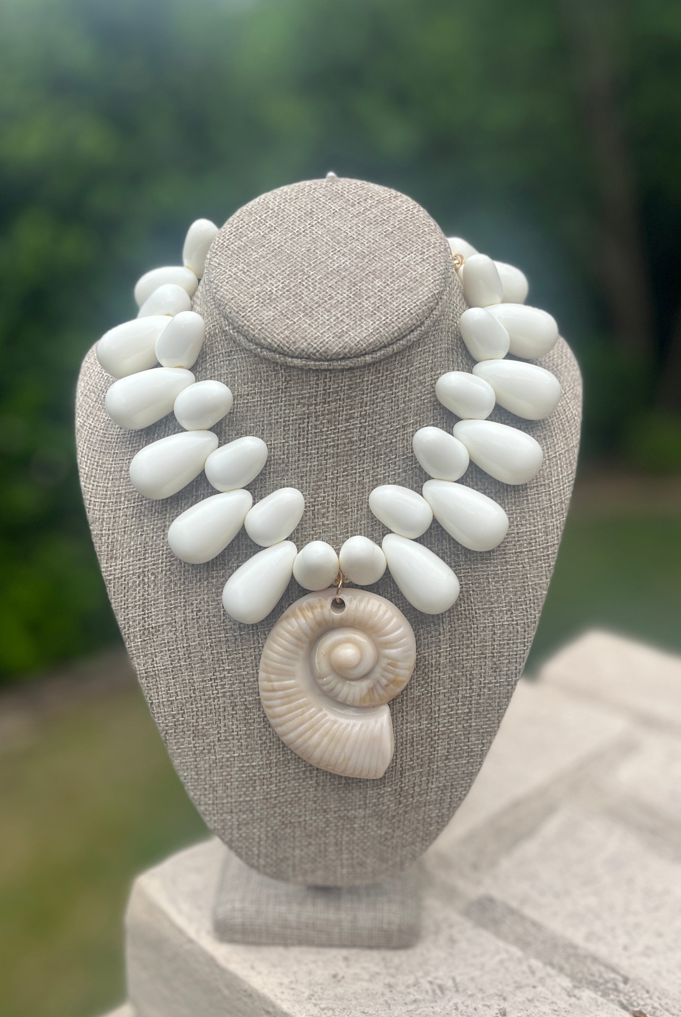 Necklace with white stones and a shell on a gray stand against a blurred green background