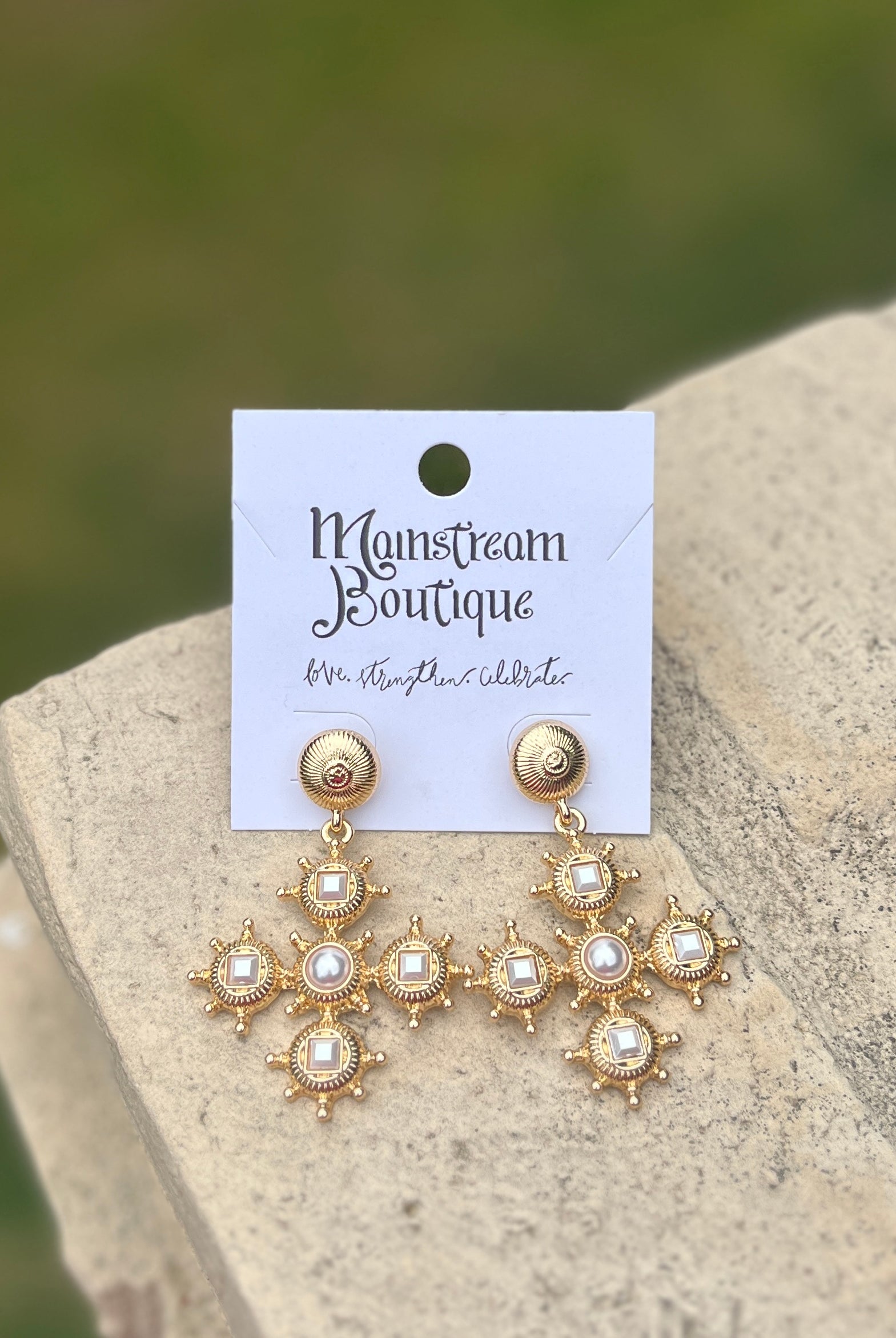 Gold and pearl earrings placed on a stone surface.