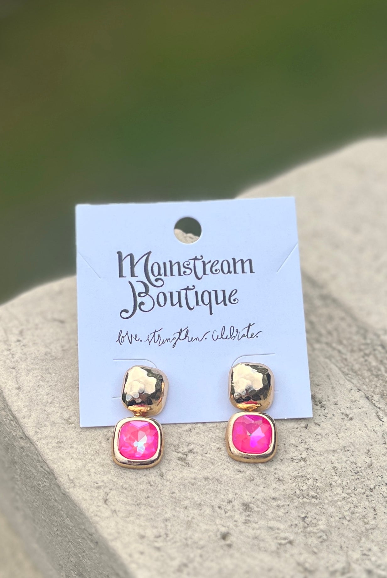 Pair of gold and pink stone earrings against a blurred natural background.