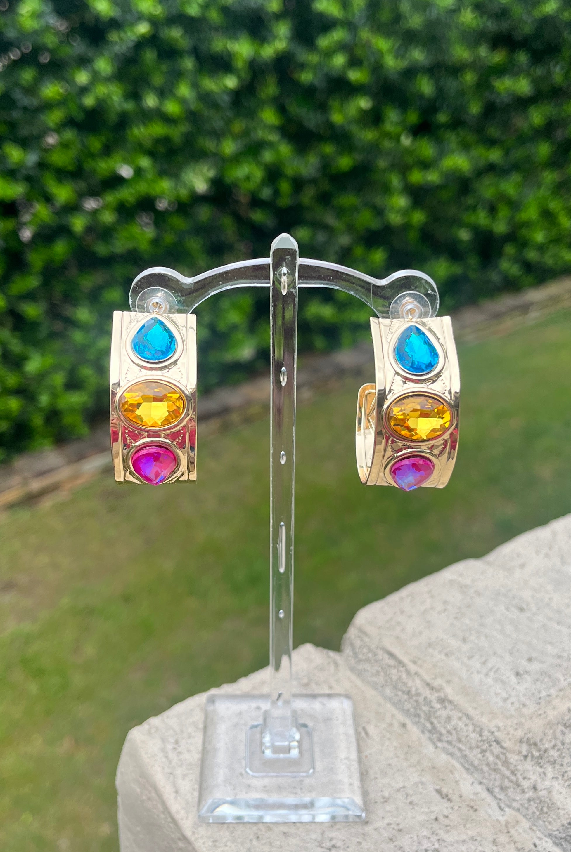 Colorful gemstone earrings on a stand with a green outdoor background