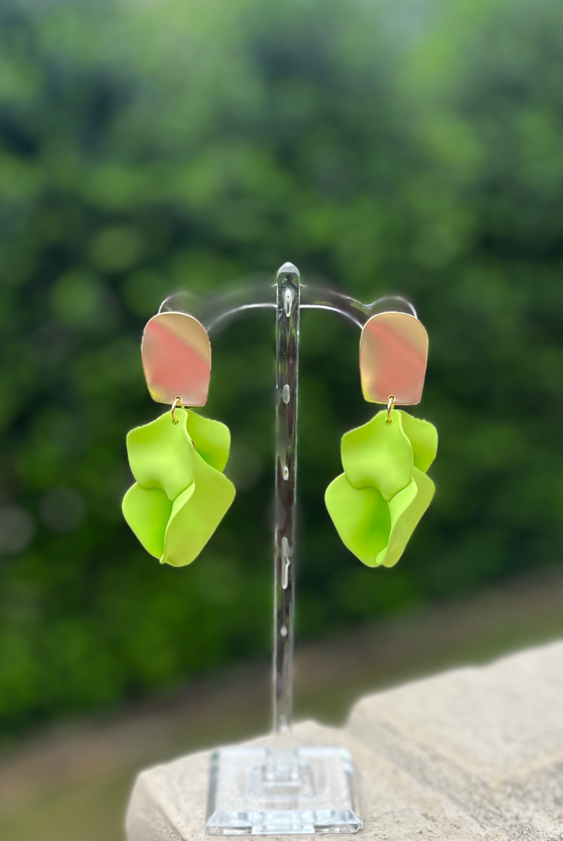 Pair of green flower-shaped earrings on a stand with a blurred green background