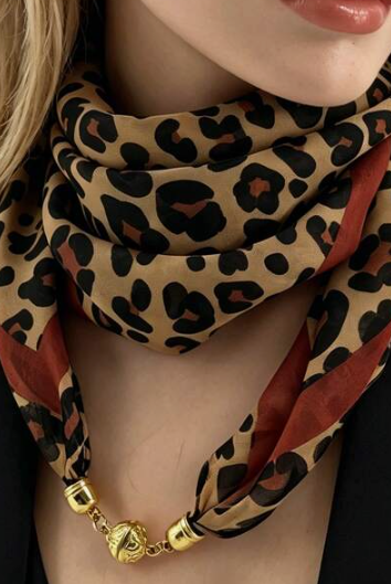 A close-up of a model wearing a leopard print scarf with rust red stripes and gold-toned chain links at the bottom.