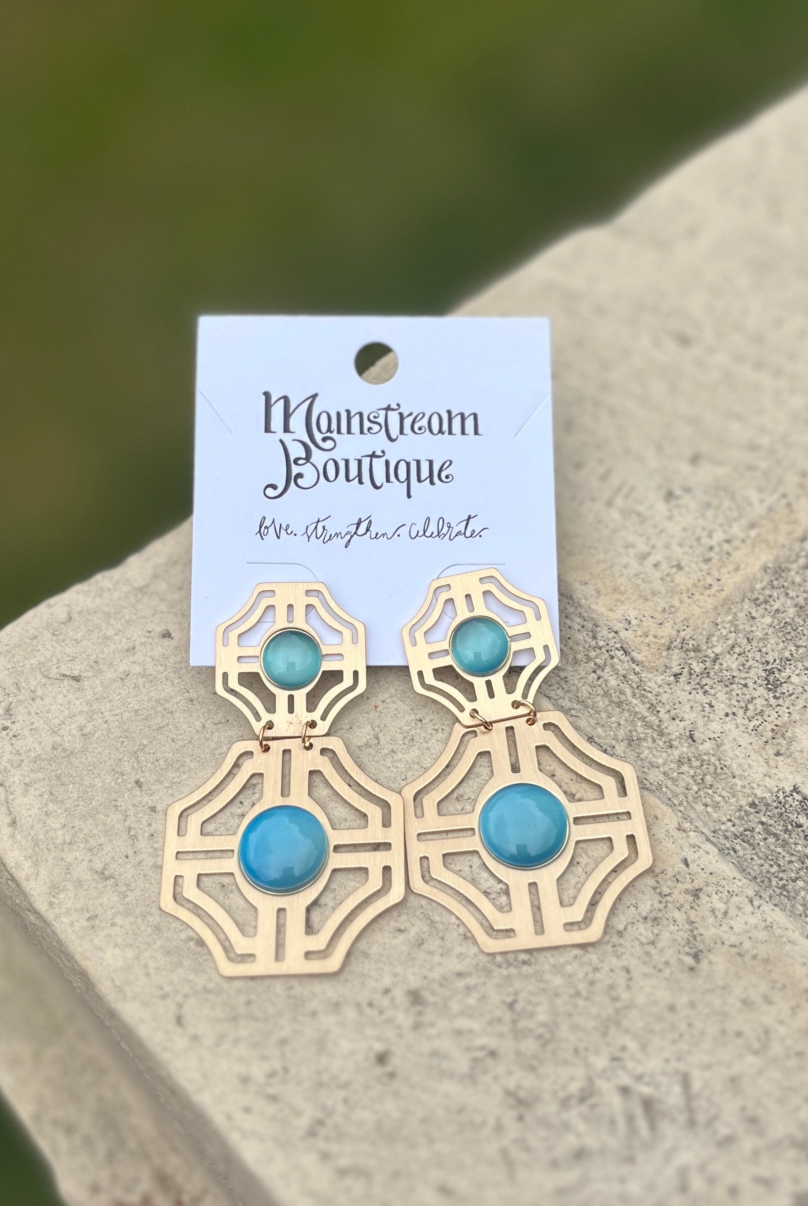 Gold earrings with blue stones placed on a stone surface.