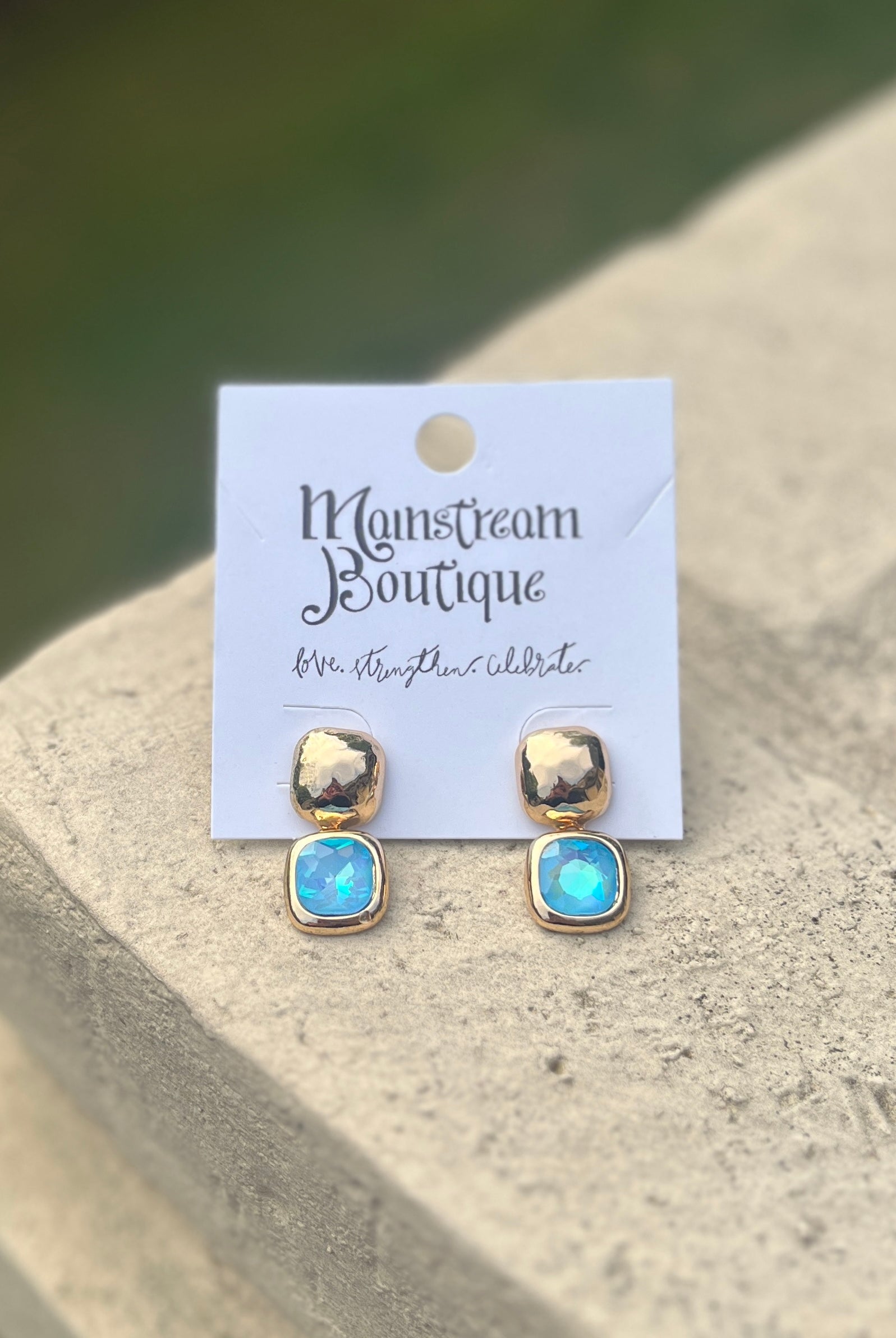 Pair of gold and blue earrings against a stone surface.
