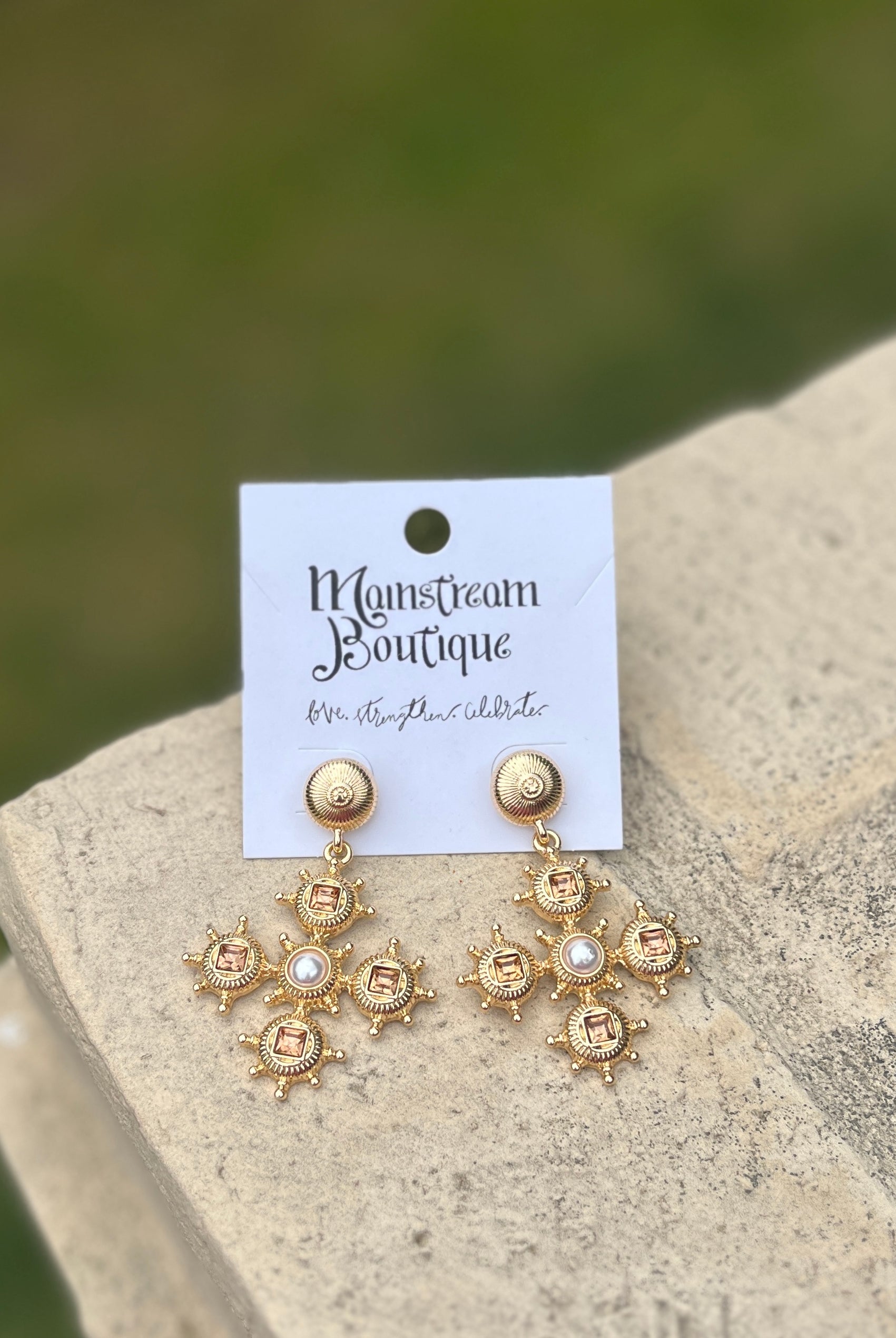 Gold earrings with topaz stones and pearl-like centers on a stone surface.