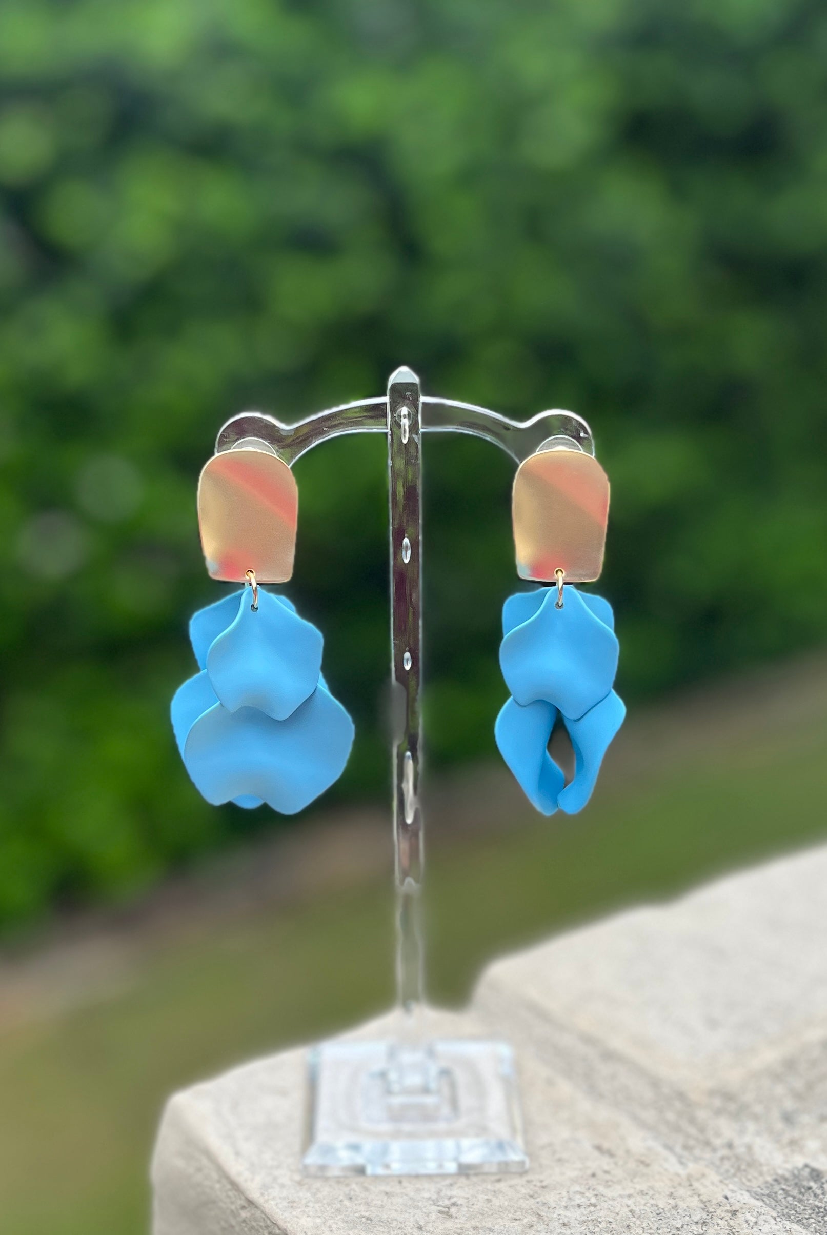 Blue floral earrings on a clear stand with a blurred green background