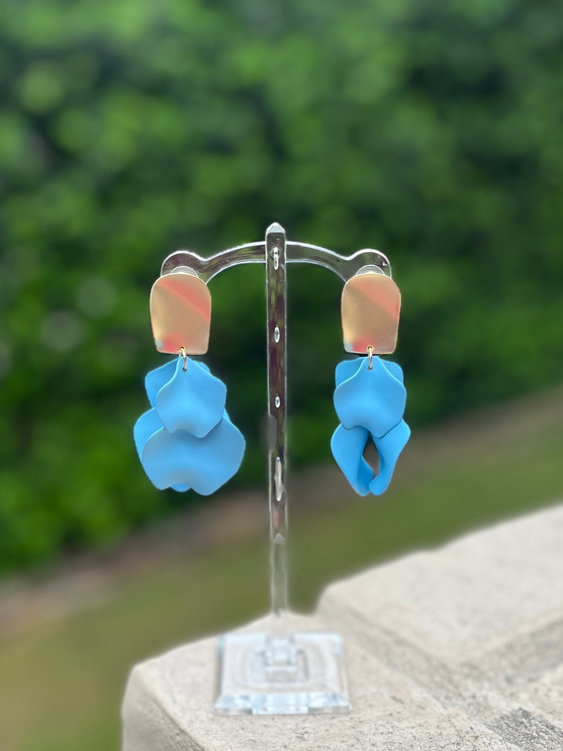 Blue floral earrings on a clear stand with a blurred green background