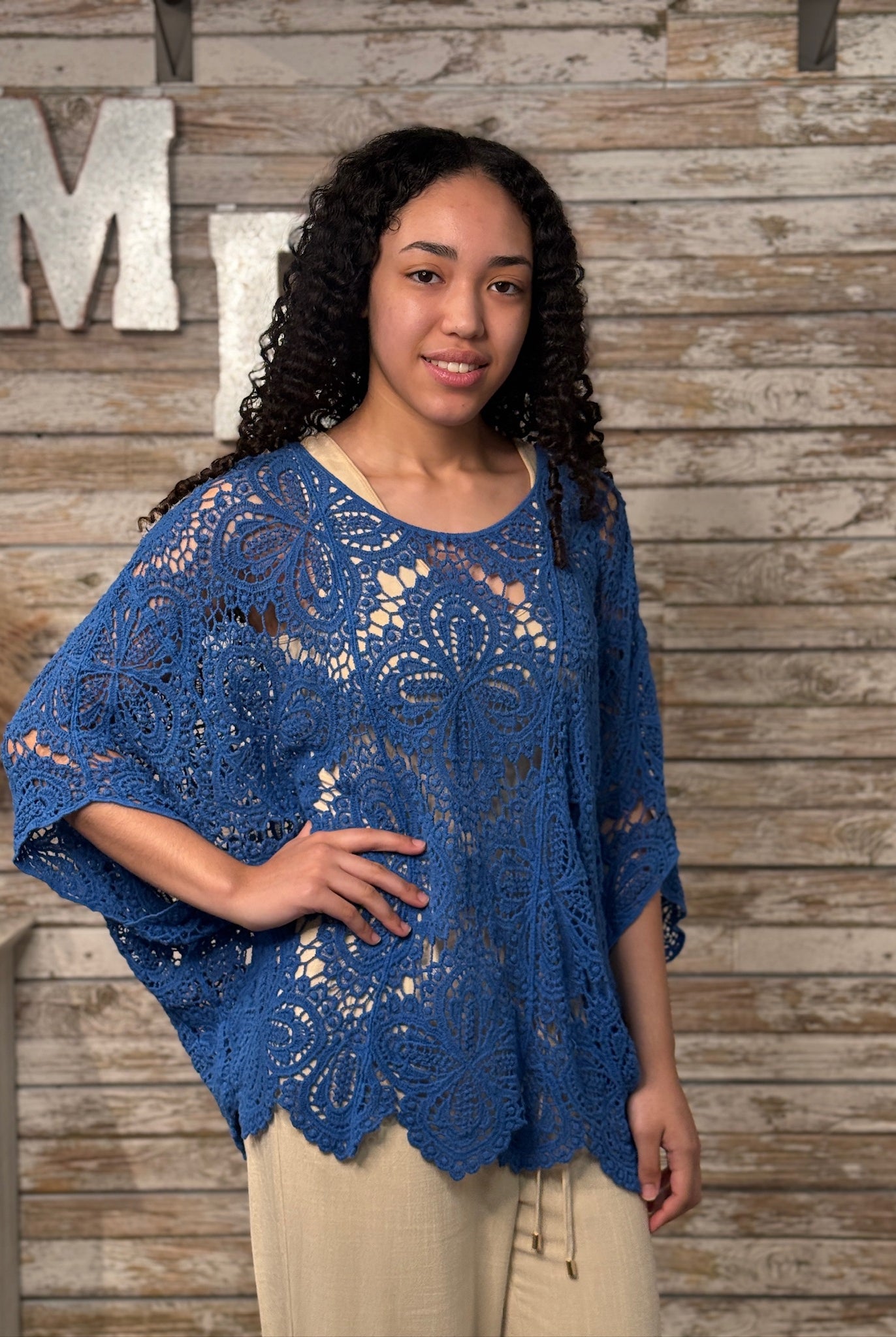 Woman wearing a blue crochet lace top against a wooden wall.