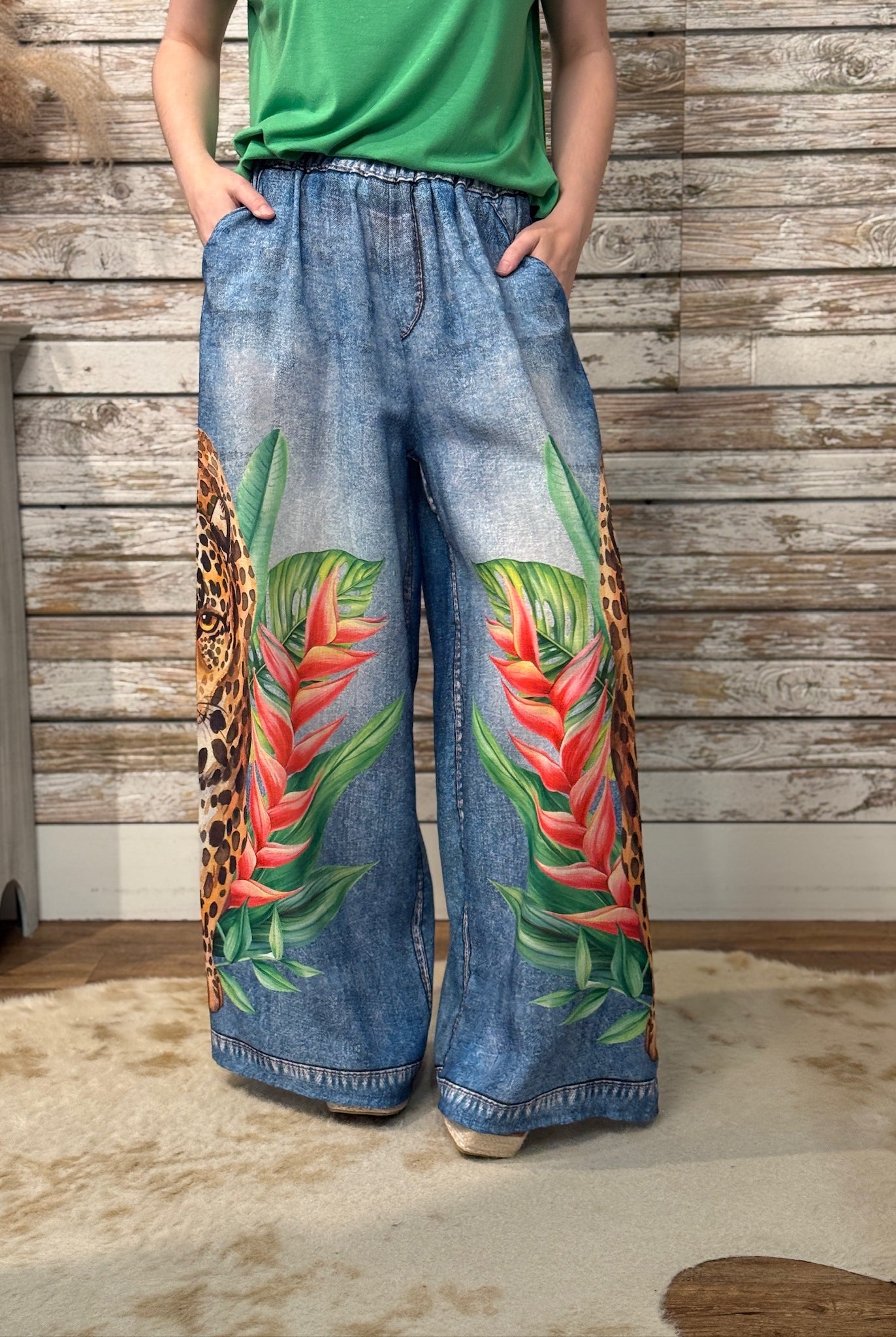 Person wearing blue jeans with tropical leaf design against a wooden wall.
