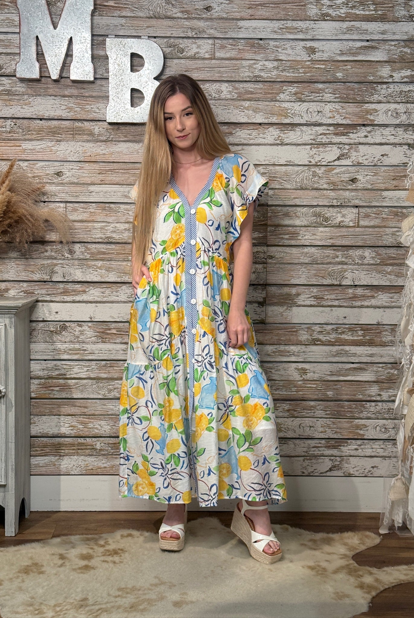 Woman wearing a floral dress standing against a wooden wall with decorative elements.