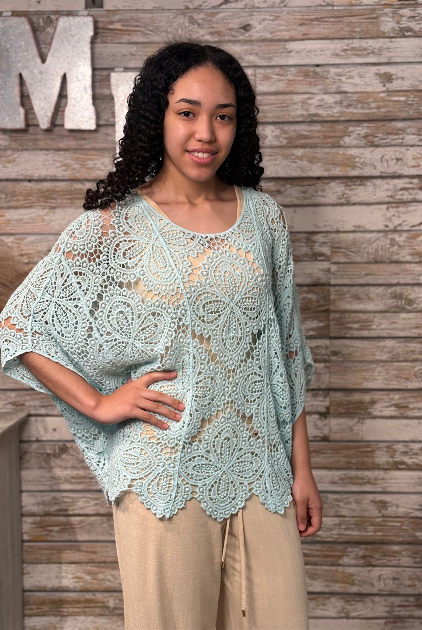 Woman wearing a light blue crochet lace top against a wooden background