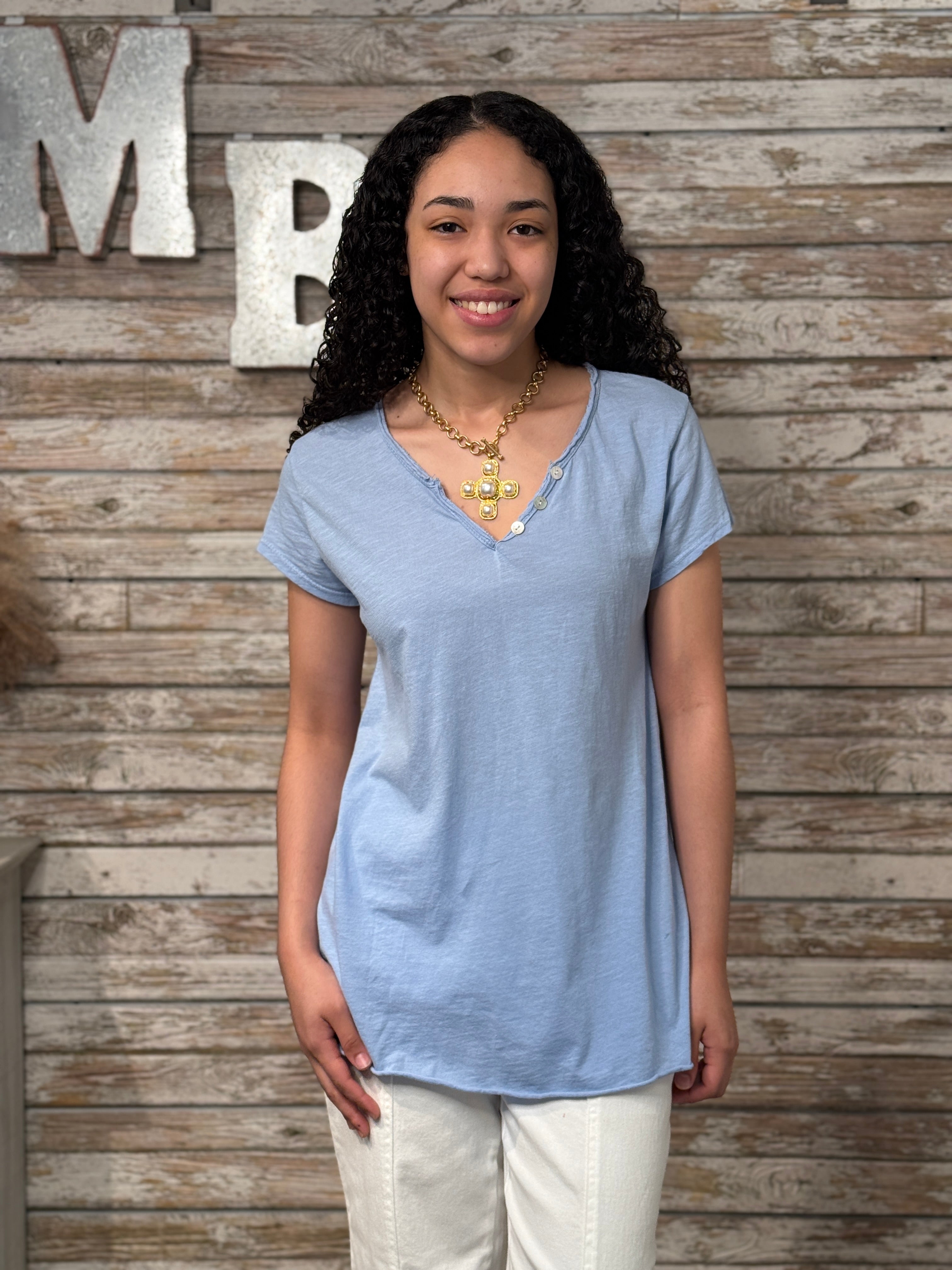 Woman wearing a blue shirt and white pants standing against a wooden wall with decorative letters.