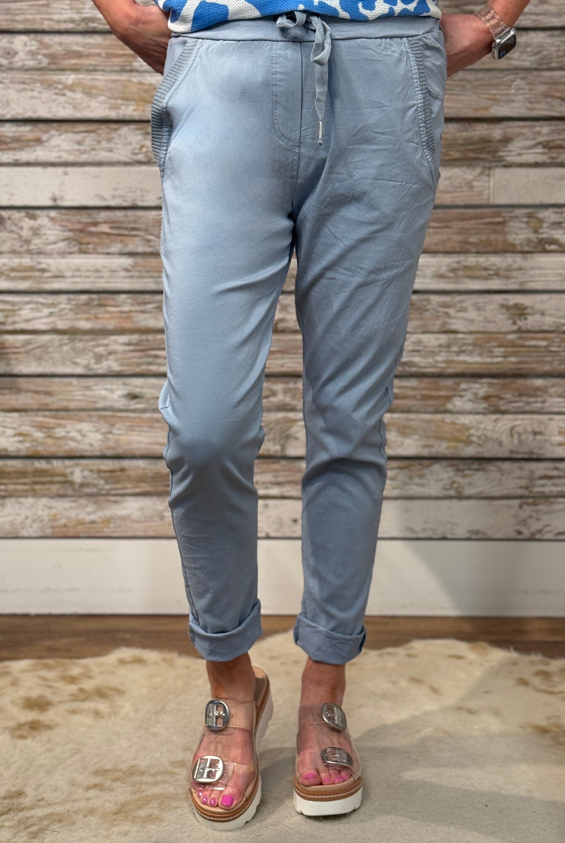 Person wearing light blue jogger pants standing against a wooden wall.