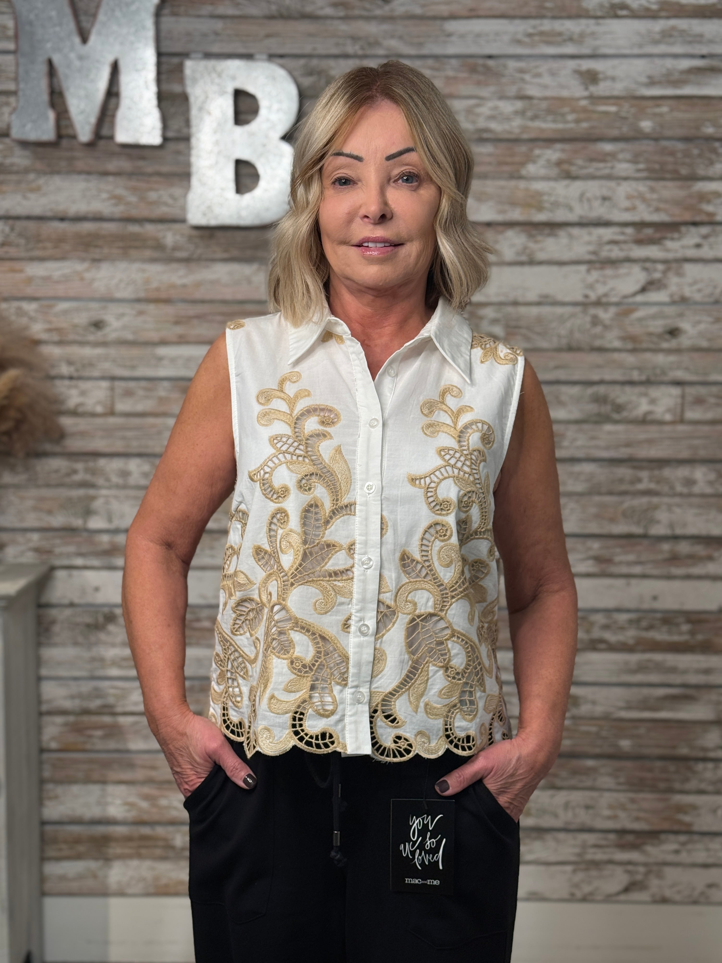 Woman wearing a white blouse with gold embroidery against a wooden wall.