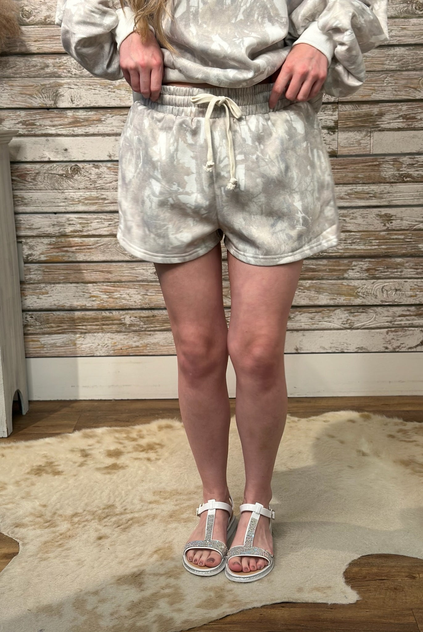 Person wearing a camo outfit with shorts and a top, standing against a wooden wall.