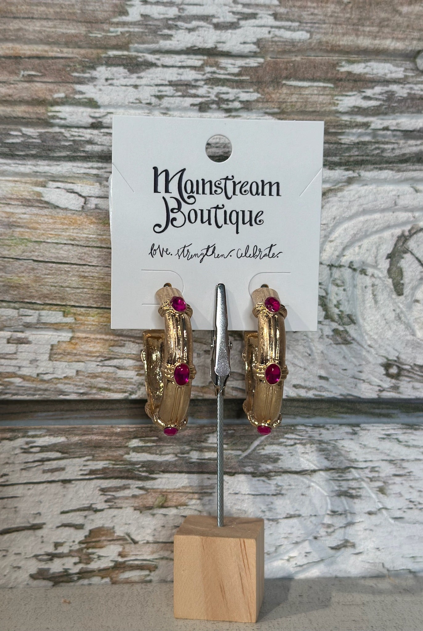 Gold hoop earrings with fuschsia stones on a stand against a rustic wooden background
