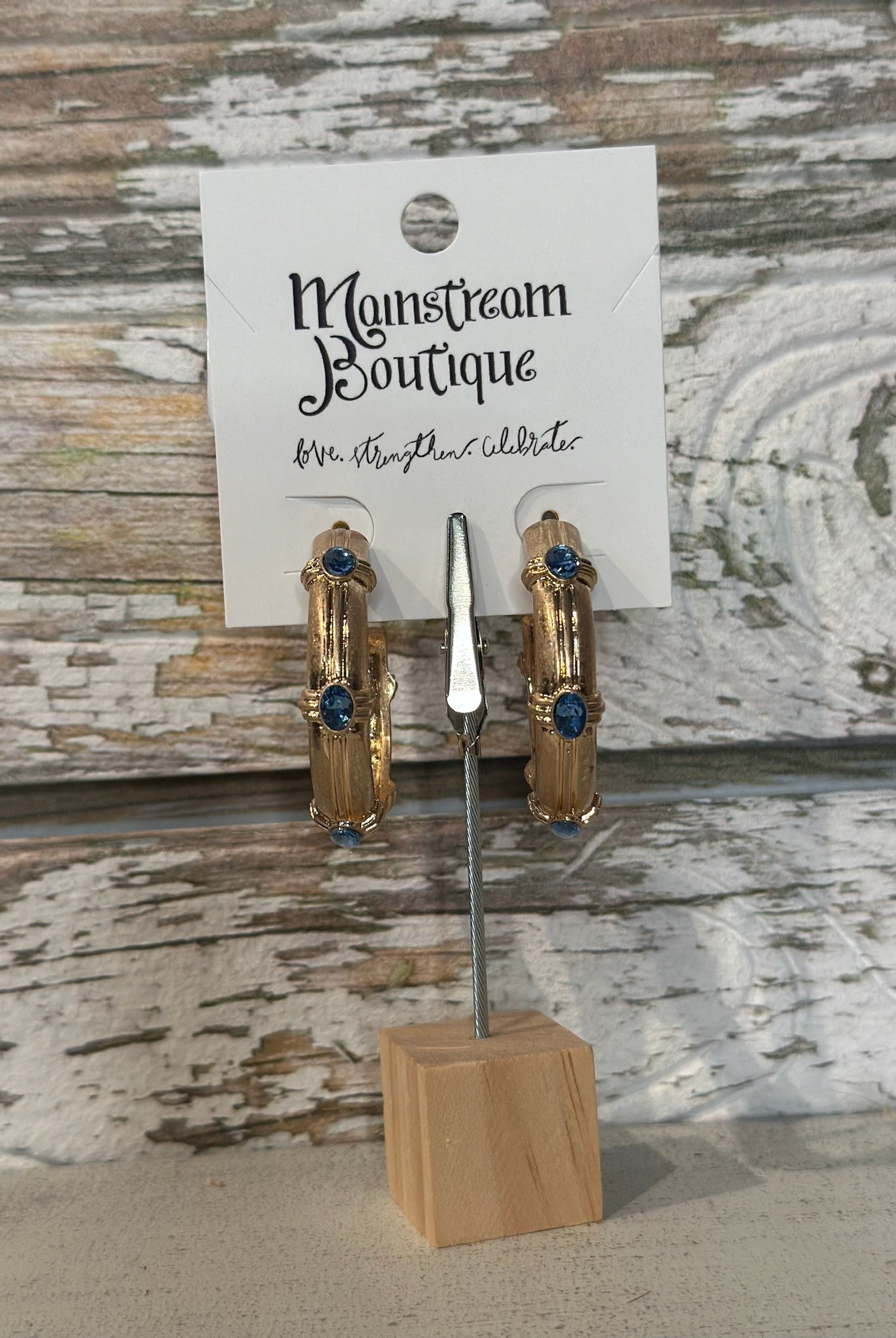 Gold hoop earrings with blue stones on a wooden stand against a rustic wooden background.