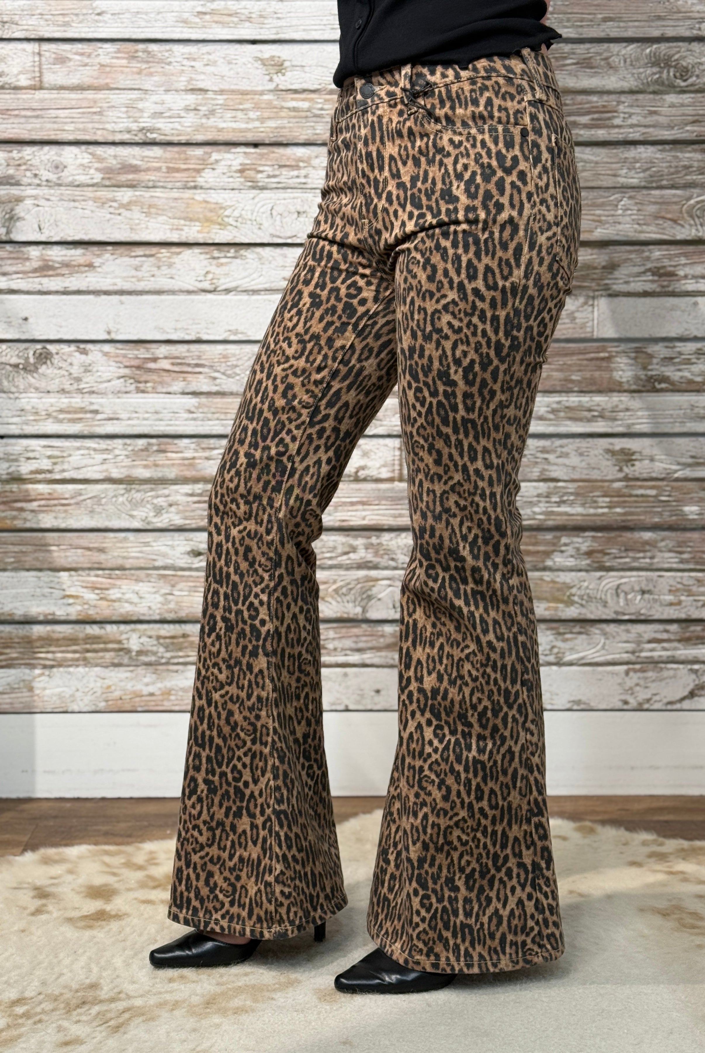 Leopard print bell-bottom pants worn by a person against a wooden wall.