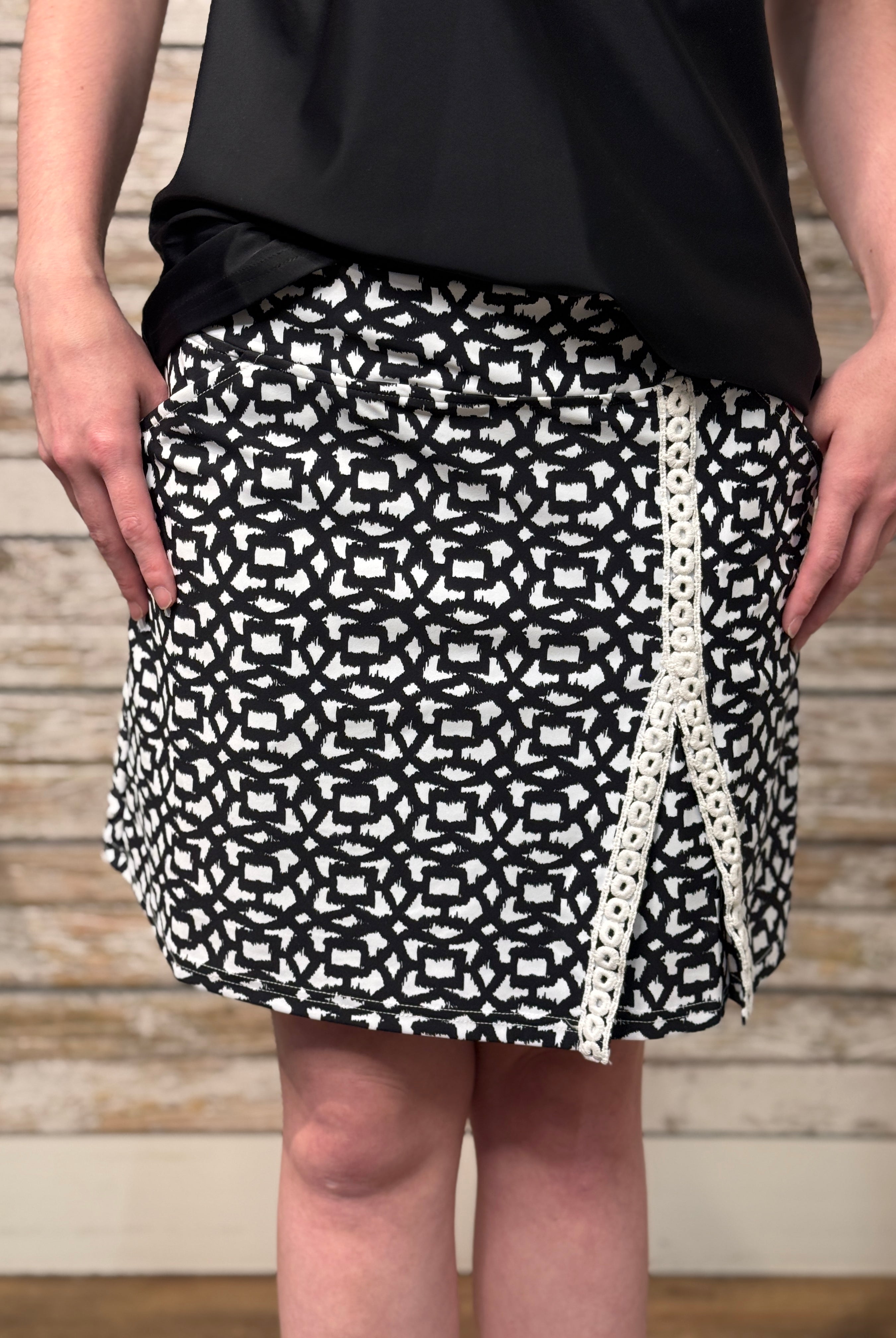 Person wearing a black and white patterned skirt with a wooden background