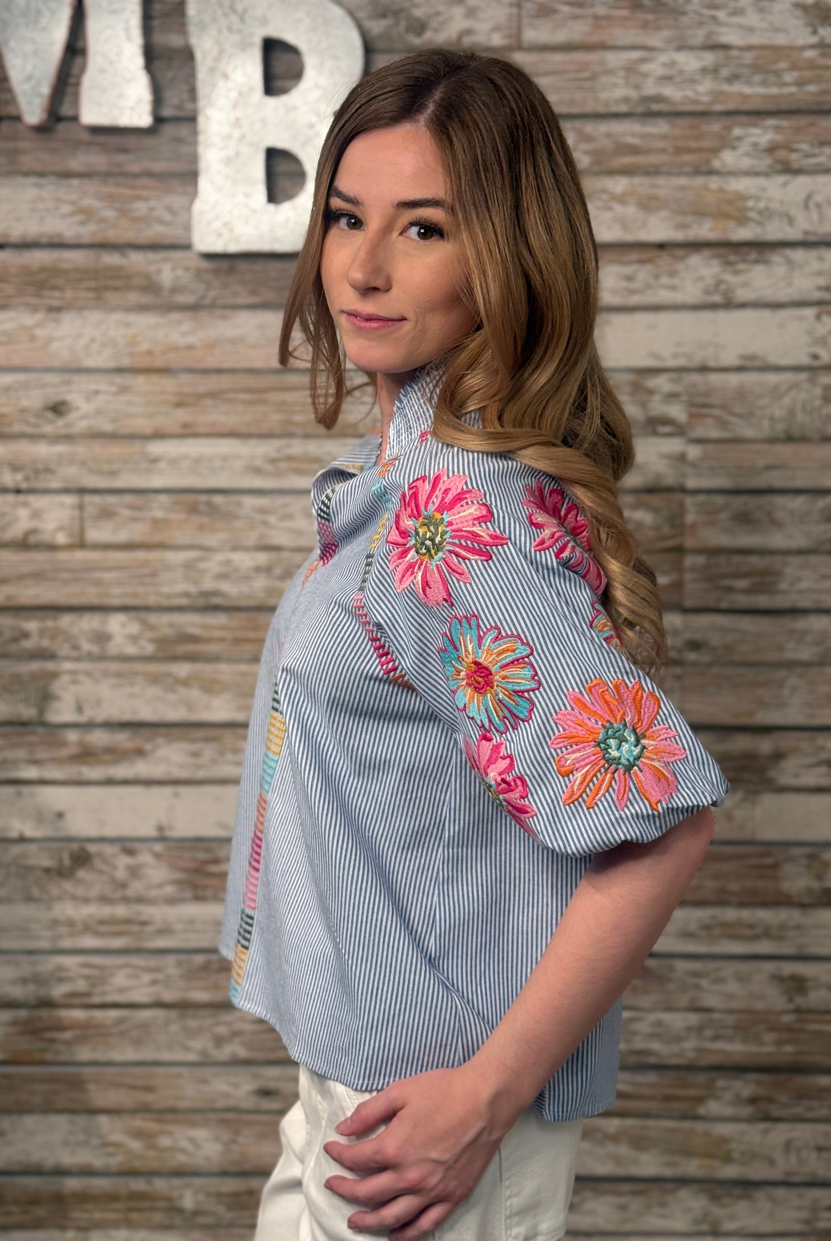 Woman wearing a blue shirt with floral embroidery against a wooden background