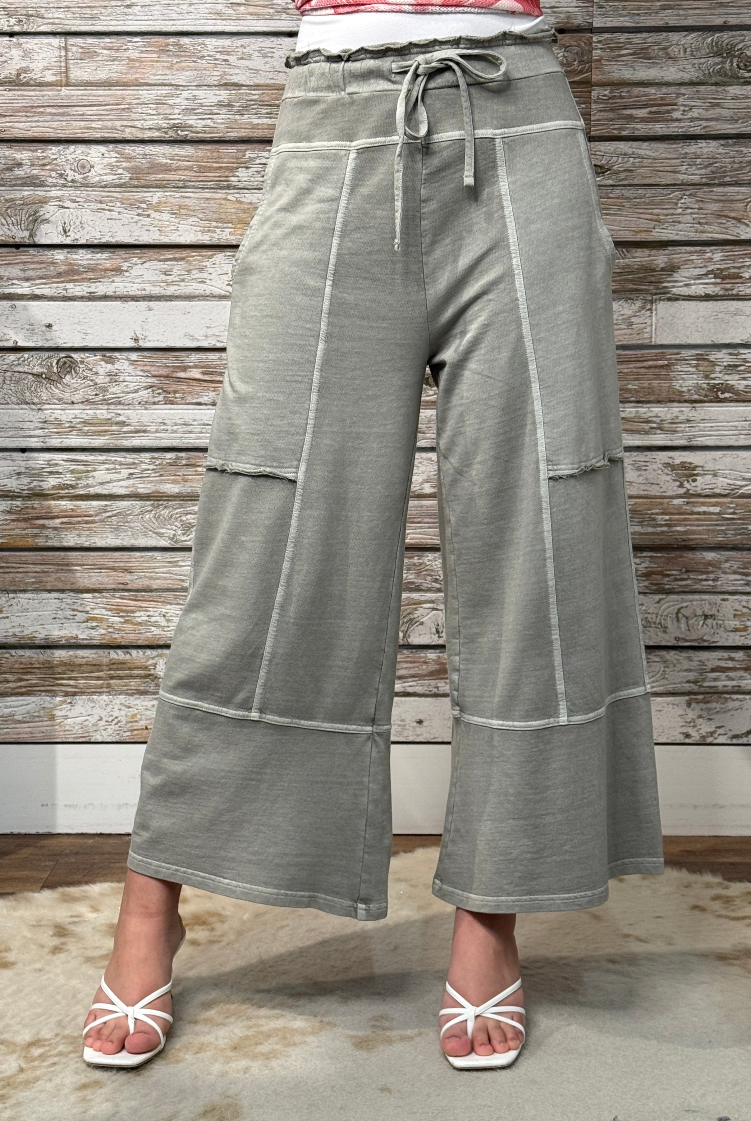 Person wearing gray wide-leg pants with a wooden wall background