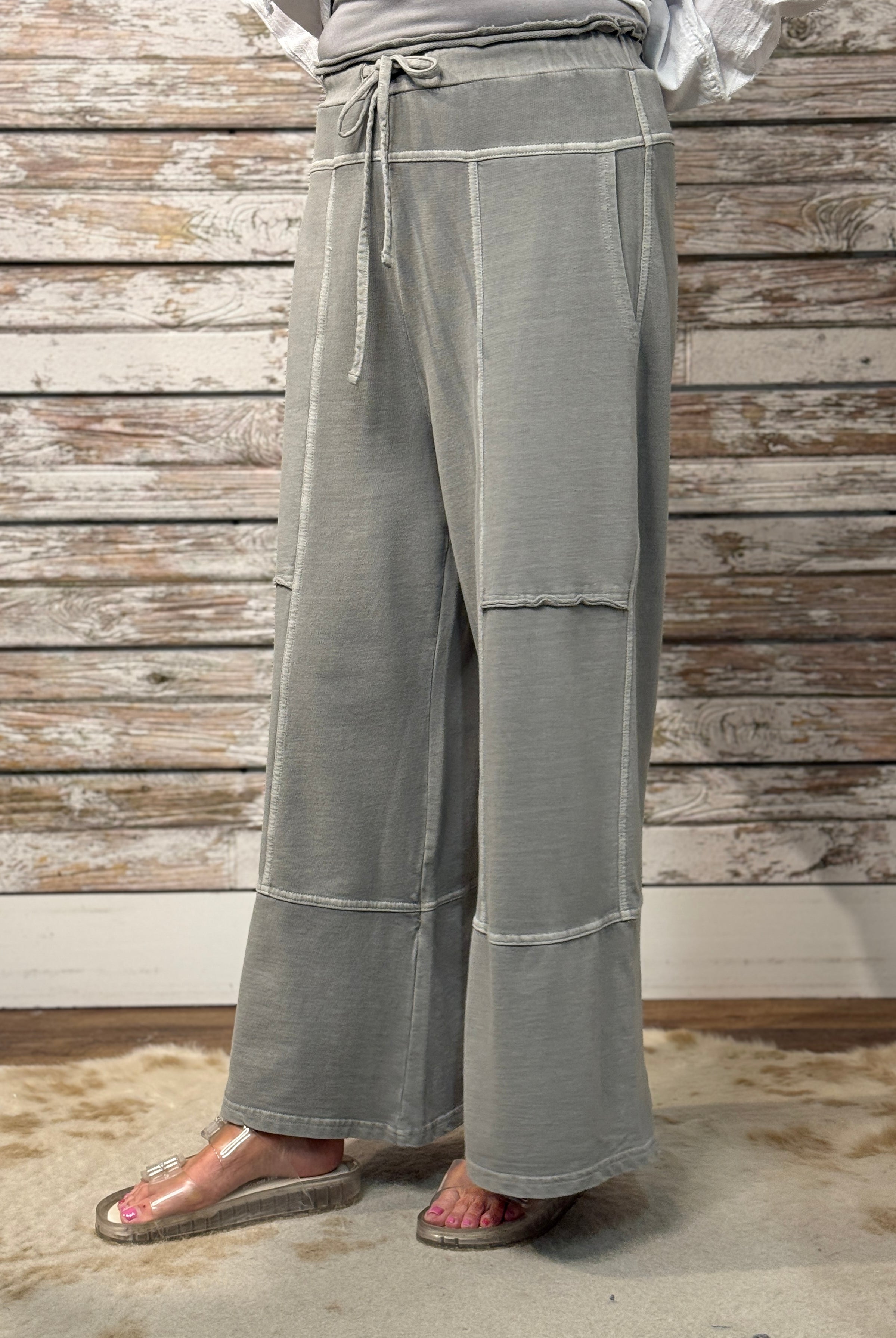 Person wearing gray wide-leg pants against a wooden wall.