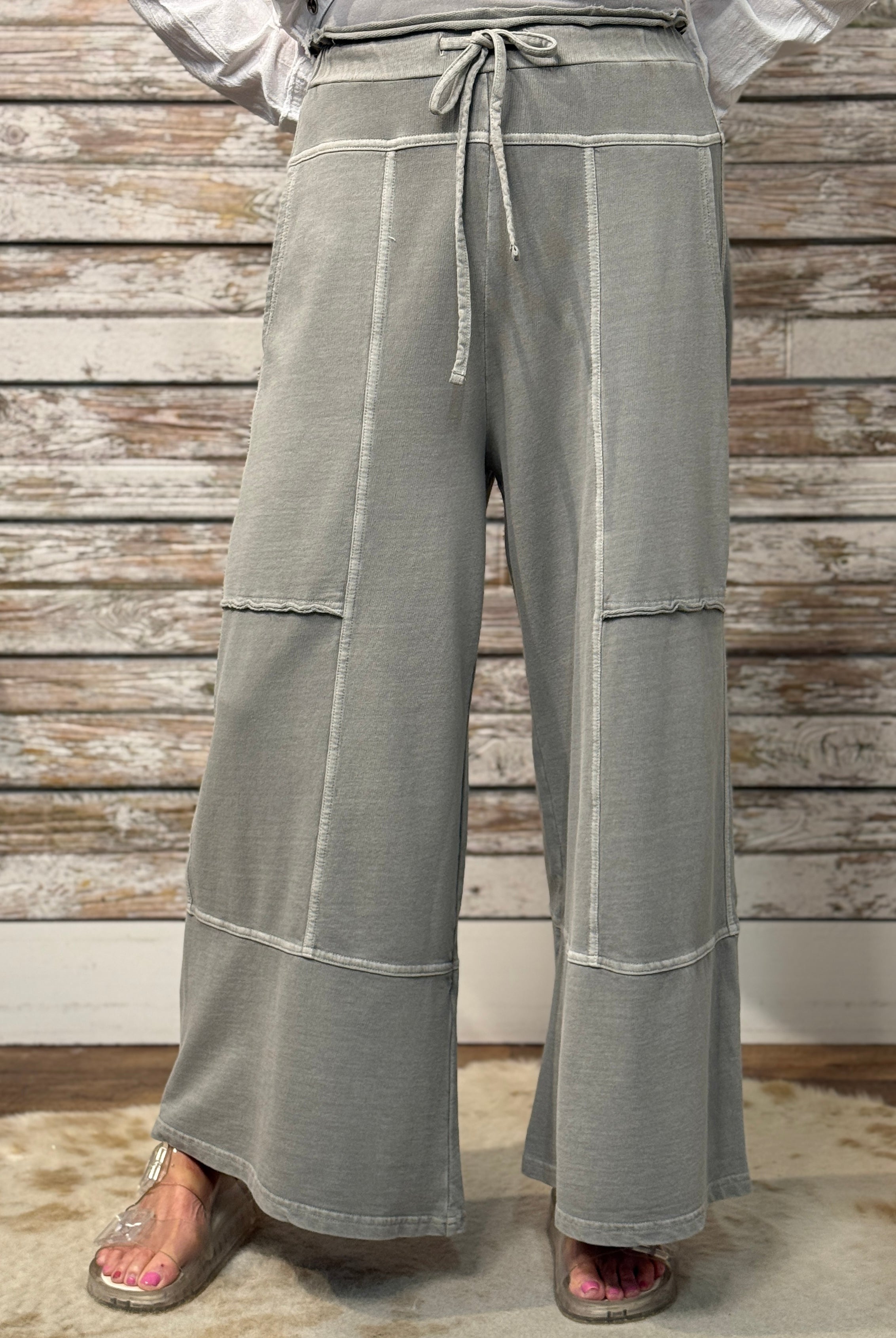Gray wide-leg pants with white stripes worn by a person against a wooden wall.