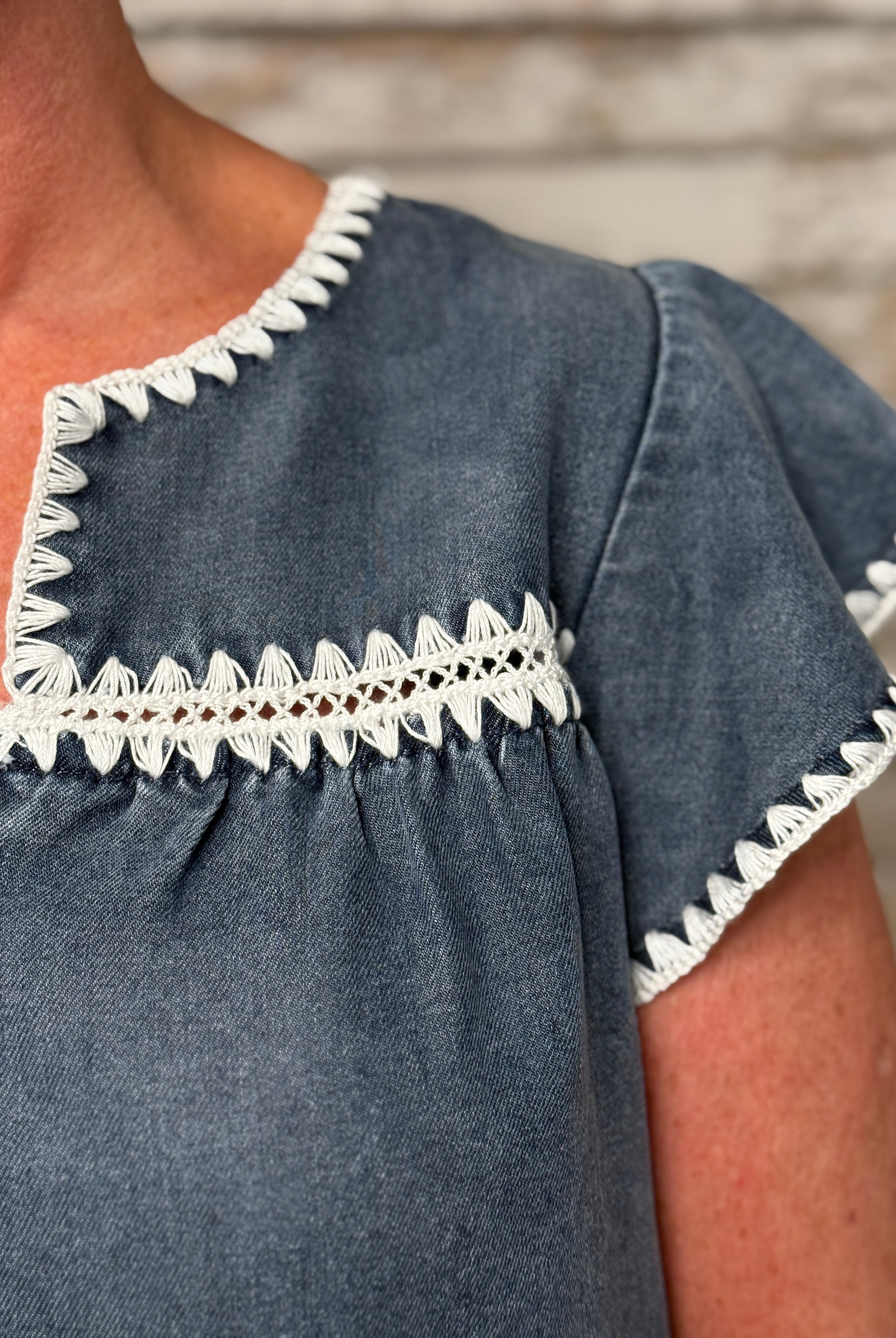 Blue dress with white lace trim worn by a person, against a wooden background.