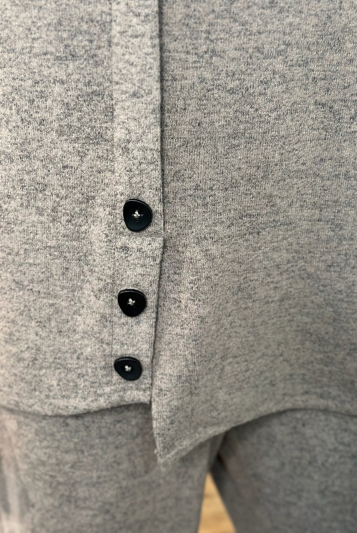 Close-up of a knit garment with three black buttons down the front, showing the fabric texture and button details.