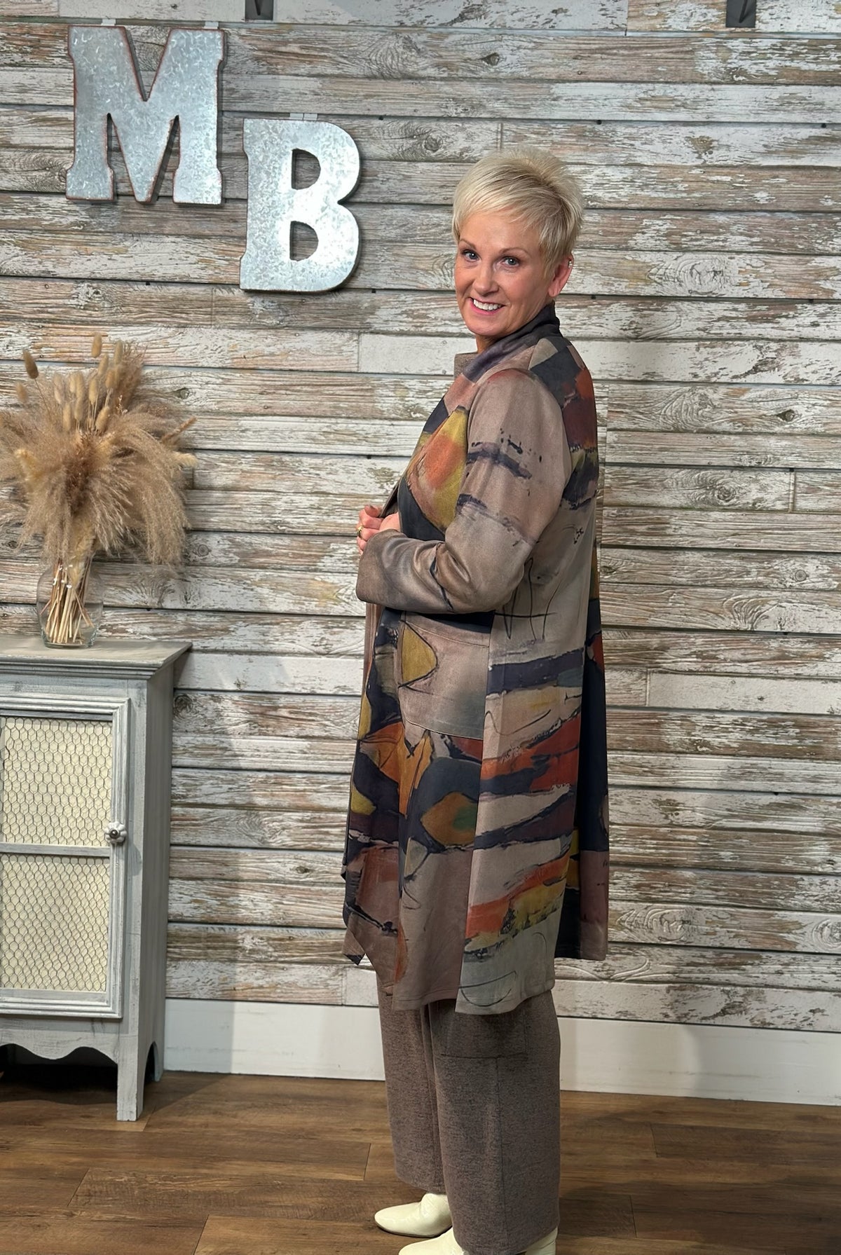 A woman wearing a long-sleeved abstract print cardigan over a brown top and matching pants.