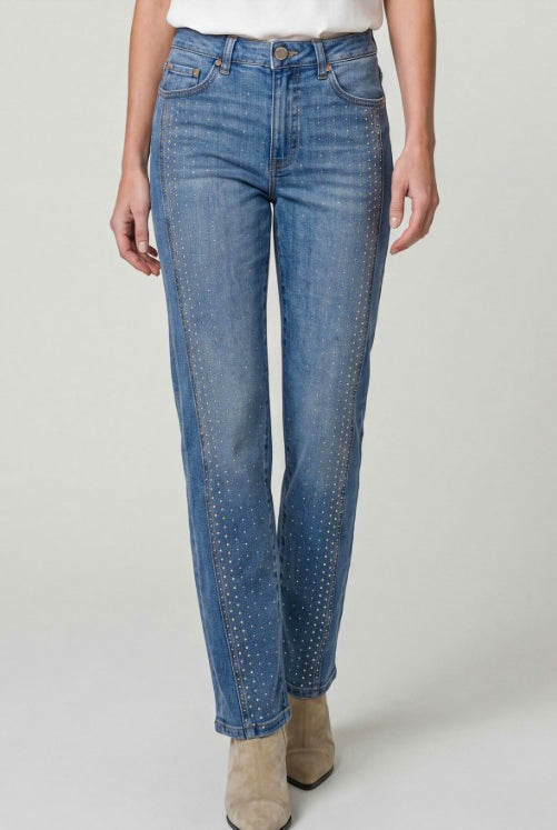 Person wearing blue jeans with gold studs on a plain background