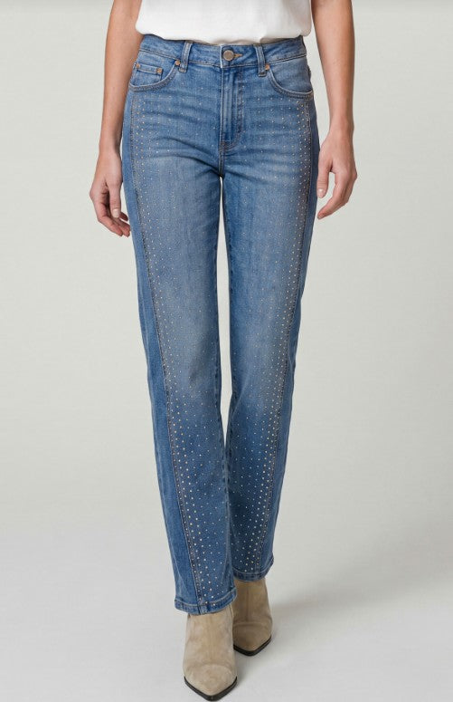 Person wearing blue jeans with gold studs on a plain background