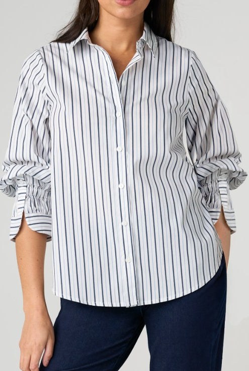 Person wearing a white and Navy striped shirt with rolled-up sleeves on a plain background