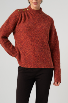 A woman wearing a textured, heathered rust-orange mock-neck sweater with decorative buttons on the shoulder, paired with black pants, against a light gray studio background.