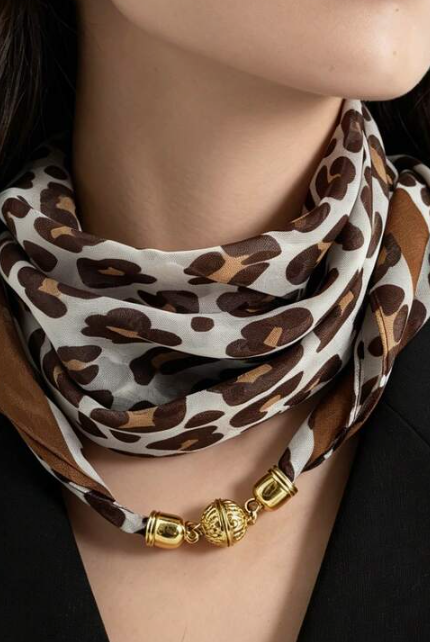 A close-up of a model wearing a leopard print silk scarf with a gold chain link necklace.