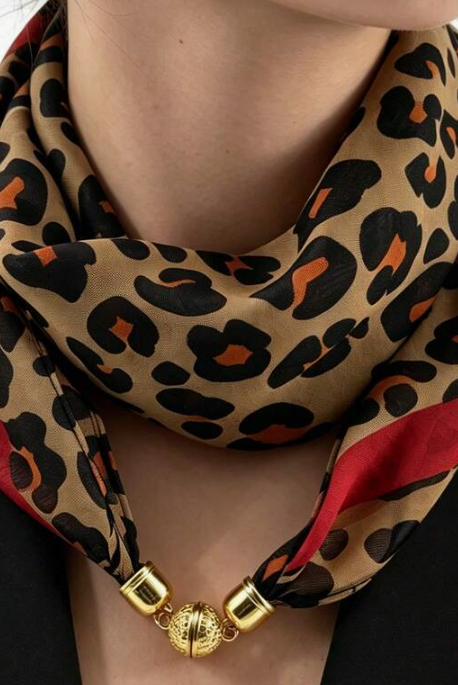 A close-up of a model wearing a leopard print scarf with red side panels and gold metal clasp details, styled with a black blazer.