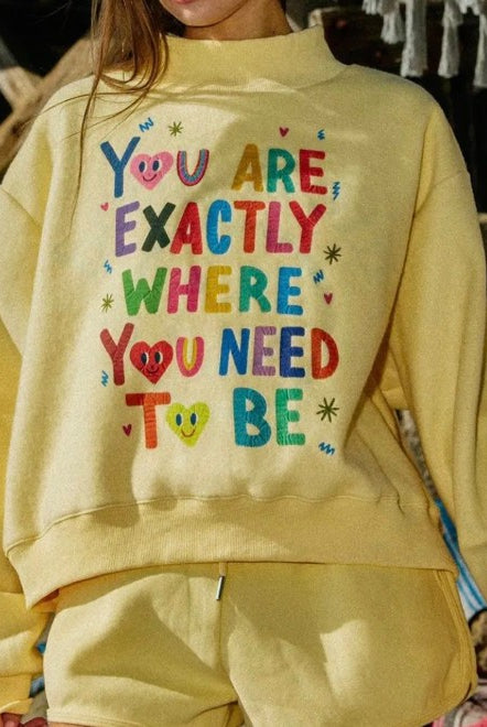 Person wearing a yellow sweatshirt with colorful text in an outdoor setting